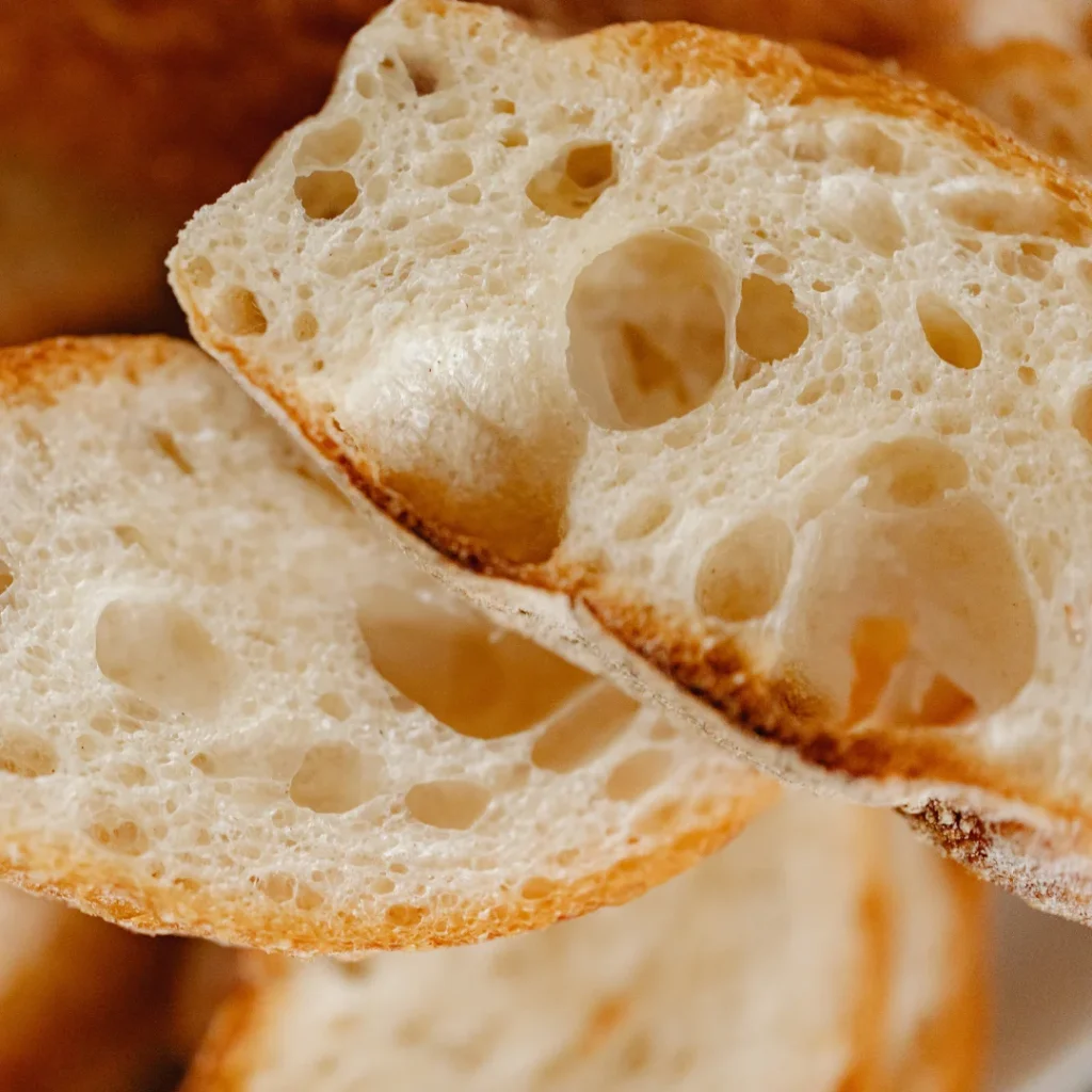 Fatias de pão rústico com furos de fermentação, mostrando uma textura aerada e macia.